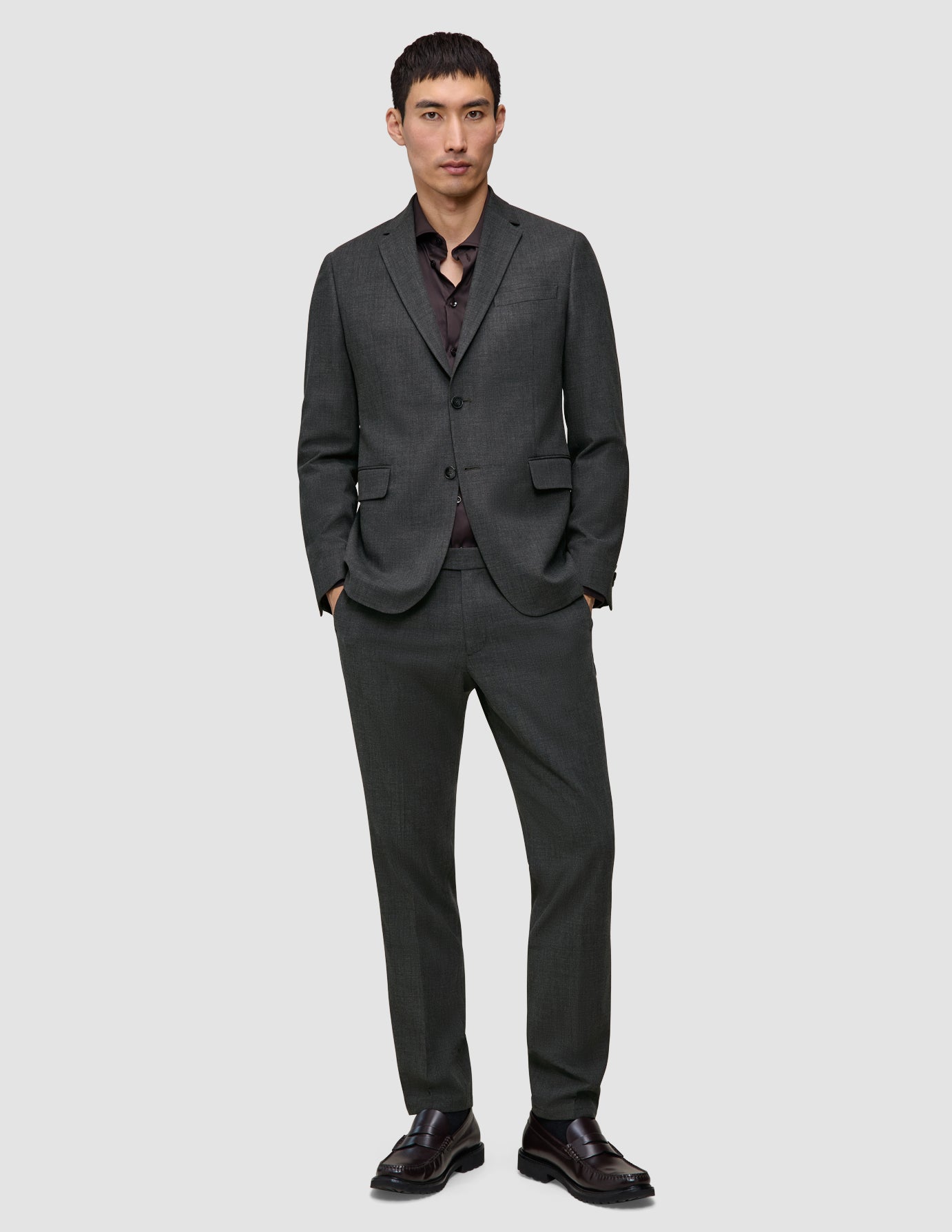 En mand iført en Motion Blazer Slim i farven Pepper Grey og matchende bukser, en mørk skjorte samt brune loafers i klassisk dansk design.